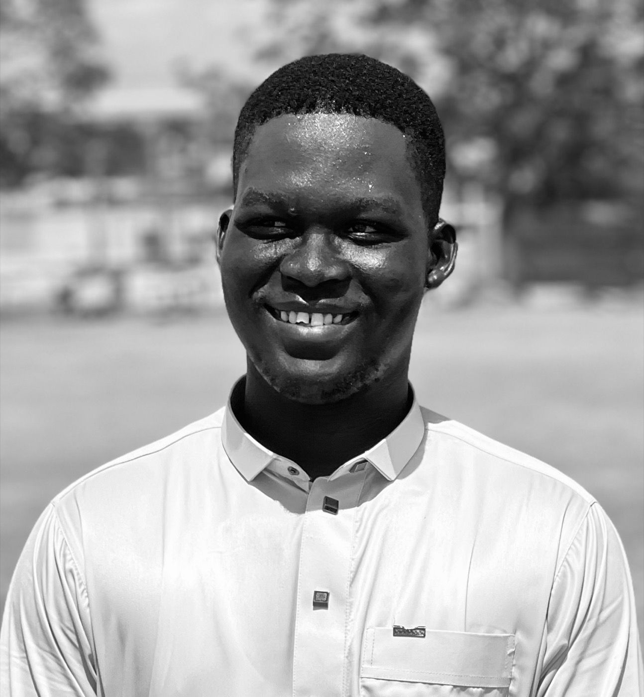 Gyen Abubakar, smiling, in a white shirt, outdoors.
